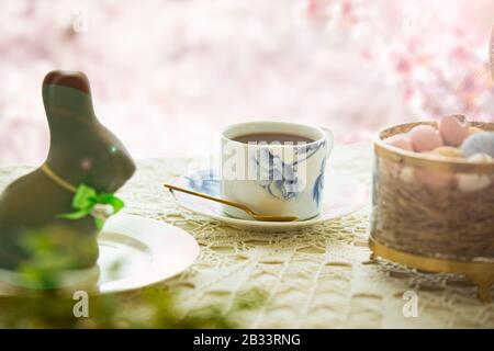Beautiful served small table with Easter decorations on outdoor terrace. Little chocolate bunny with bow, chocolate eggs, cup of coffee, crystal bowl. Stock Photo