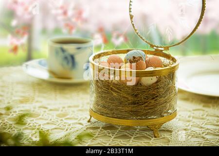 Beautiful served small table with Easter decorations on outdoor terrace. Little chocolate bunny with bow, chocolate eggs, cup of coffee, crystal bowl. Stock Photo