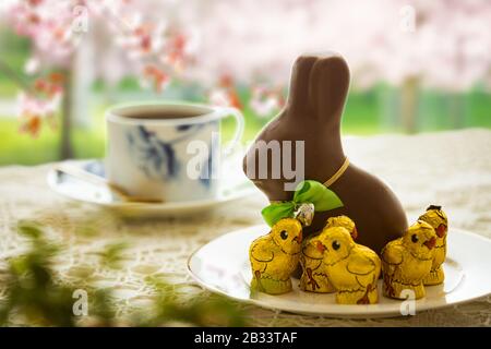 Beautiful served small table with Easter decorations on outdoor terrace. Little chocolate bunny with bow, chocolate eggs, cup of coffee, crystal bowl. Stock Photo