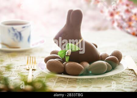 Beautiful served small table with Easter decorations on outdoor terrace. Little chocolate bunny with bow, chocolate eggs, cup of coffee, crystal bowl. Stock Photo