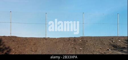 A fence made of metal mesh separates the  sandy quarry pit and the blue sky. Panoramic collage from several outdoor photos Stock Photo