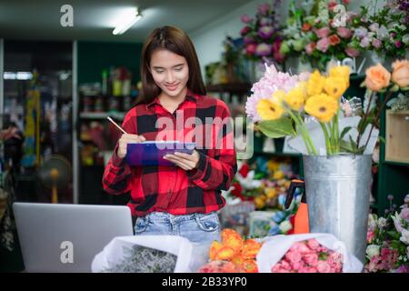 Asian Woman Florist Small Business Flower Shop Owner and She is using her telephone and laptop to take orders for her store. Stock Photo