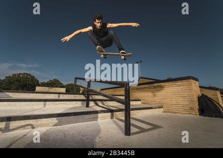 Low angle shot of a Caucasian athletic male in a black outfit doing a flip trick with a skateboard Stock Photo