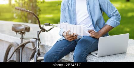 Unrecognizable black man stopped his bike in park and checking documents Stock Photo