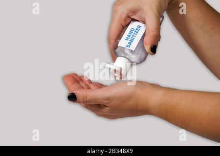 Cleaning hands with waterless, alcohol-based hand sanitizer antiseptic gel. Female holds bottle for handrubs & pours liquid used as hand disinfectant. Stock Photo