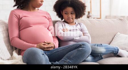 Upset little girl looking at pregnant mother belly with jealousy Stock Photo