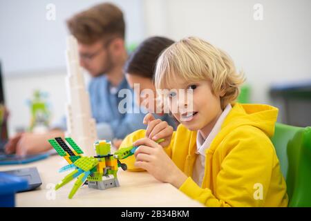 Boy playing with buildable bird, girl and teacher sitting next to him Stock Photo