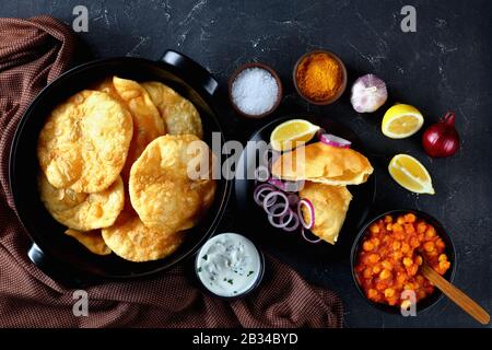 chole Bhature, a popular combo of puffed fried leavened bread and chickpea curry on a concrete table with lemon and frsh onion rings, horizontal view Stock Photo