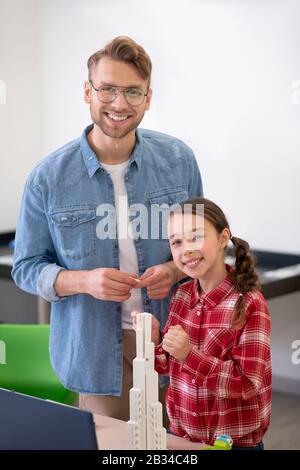 Teacher and girl standing near buildable tower, smiling Stock Photo