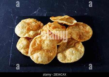 Bhatura, indian deep fried leavened bread on a black slate tray on a concrete table, horizontal view from above, close-up Stock Photo