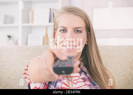 Beautiful young woman holding tv remote control and changing TV channels Stock Photo