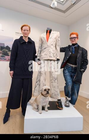 London, UK.  4 March 2020. Tilda Swinton (L) and Academy-Award winning costume designer Sandy Powell (and Juno the dog) with her suit, on display ahead of being offered for auction at Phillips, Berkeley Square.  Worn by Powell at the 2020 BAFTAs and Oscars, the cream calico toile suit includes autographs from over 100 movie stars.   Proceeds will go towards Art Fund's public appeal to save and protect Prospect Cottage in Dungeness, Kent, home of filmmaker Derek Jarman. Credit: Stephen Chung/Alamy Live News Stock Photo