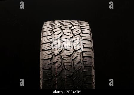 mud tire, universal off- road all terrain tread with large blocks and ground hooks. Close- up, front view on a black background. Stock Photo