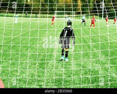 Young soccer players team on playground viewed through gate net. Stock Photo