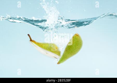 Pear cut in half falling into clear water with splashes on blue background Stock Photo