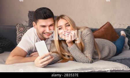 Loving young couple with mobile phone lying on sofa at home Stock Photo