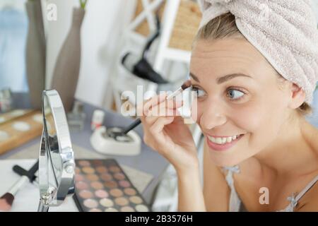 woman wearing towel on head applying make-up eyelashes Stock Photo