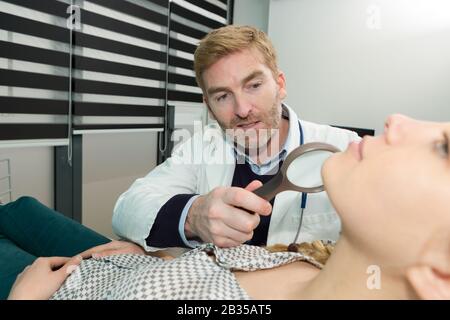 dermatologist examining mole with magnifying glass in clinic Stock Photo