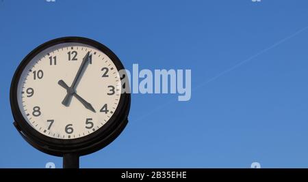 Retro style street clock on slightly blue sky background. Stock Photo