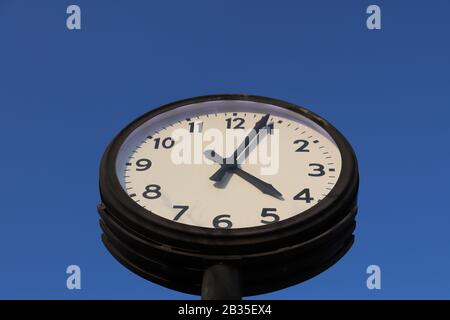 Retro style street clock on slightly blue sky background. Stock Photo