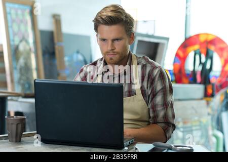 young bearded carpenter using laptop in workshop Stock Photo