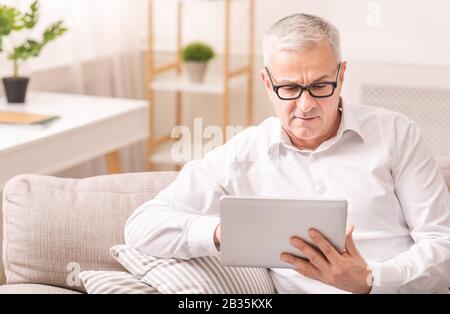 Senior man using digital tablet sitting on sofa Stock Photo