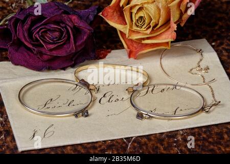 Vintage Love Letter Reading: closeup of a vintage envelope from the early 19th century on  old book cover background with historic female glasses and Stock Photo