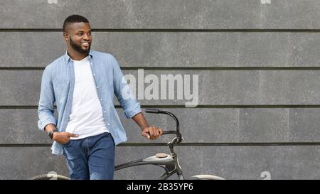 Handsome black man standing with bike against urban wall, looking away Stock Photo
