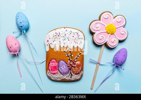 Gingerbread Easter cake and flower, colored decorative Easter eggs on sticks with ribbons on light blue background. Easter festive background. Top vie Stock Photo
