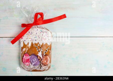 Easter festive decoration. One gingerbread Easter cake packed in cellophane with red ribbon as gift on wooden backdrop. Traditional Easter symbol. Top Stock Photo