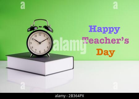 HAPPY TEACHERS DAY text, Alarm Clock and book on green background. Copy space, education and holidays concept Stock Photo