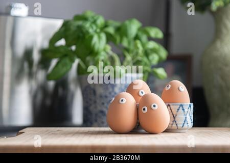 Happy Easter eggs in the kitchen among the spring grass with flowers, Easter egg hunt, egg characters with funny faces, Happy Easter concept, kitchen Stock Photo