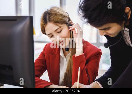 Two Asian call center operator agents working together and help each other. Concept for business, teamwork, office lifestyle. Stock Photo