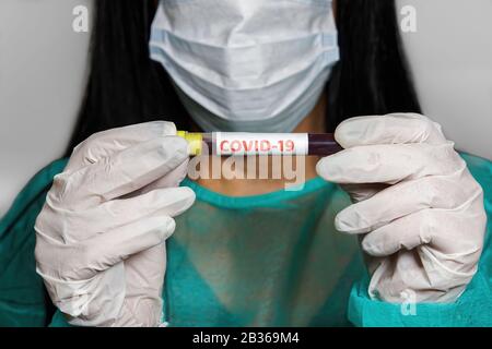 Coronavirus COVID-19 world outbreak concept. Female chemist with protective mask & gloves displays vacutainer blood tube positive on 2019-nCoV. Stock Photo