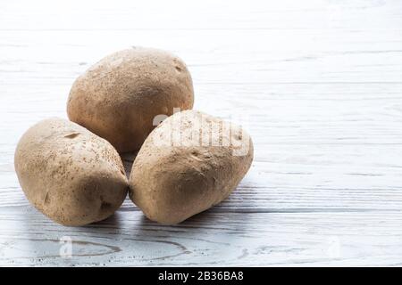 three fresh potatoes on a white wooden board. copy space Stock Photo