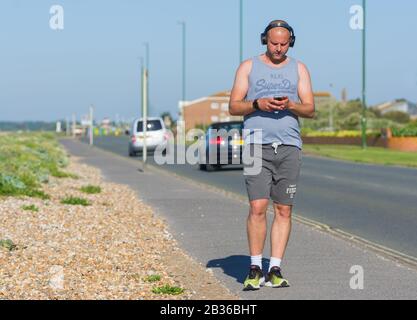 Young man walking on a warm Spring day wearing headphones listening to music. Music on the go. Portable music. Stock Photo