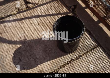 Plastic bucket on an old stone floor. Shadows from the mesh fence Stock Photo