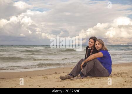 Couple sitting on the beach looking into the camera Stock Photo