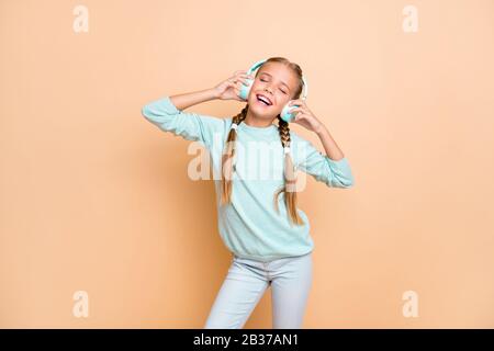 Photo of beautiful funny little lady eyes closed enjoy listen cool wireless earphones favorite song wear blue pullover jeans isolated beige pastel Stock Photo