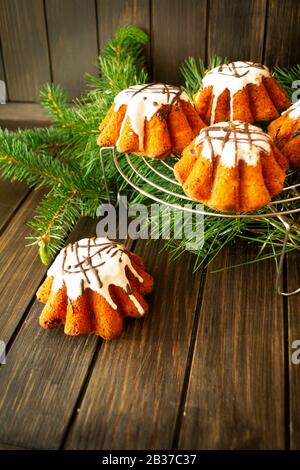 Small Christmas bundt cakes with sugar glaze on a rustic wooden table with Christmas tree on the background, copy space, vertical image Stock Photo