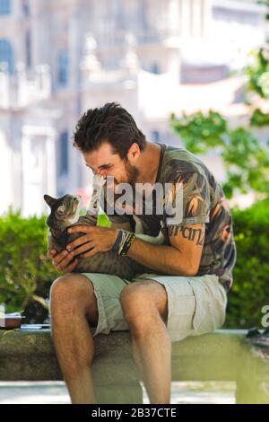 Young Man Playing With A Cat In Public Park Stock Photo