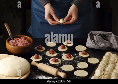 The process of making homemade dumplings. Hands of the cook in the frame. Dark background. Stock Photo