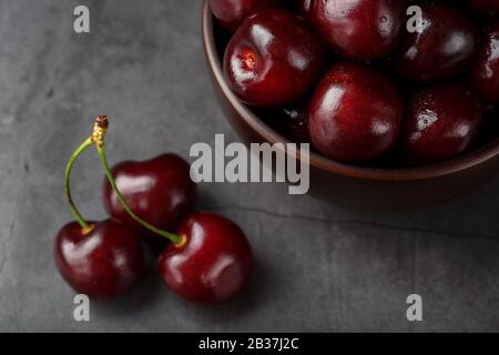 Ripe and juicy cherry berries on a black textural background in a brown cup, with water drops. Top view, close-up, Macro. Stock Photo