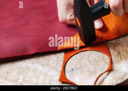 A leather craftsman produces leather goods. He taps the hammer. Handmade work. Stock Photo