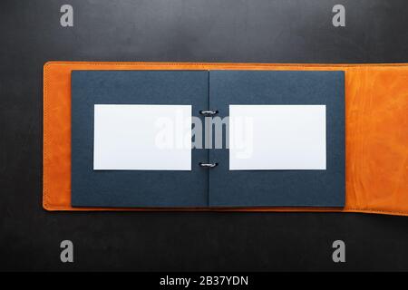 Open photo Album with empty space for photos, white frames on black paper. The album cover is made of brown handmade genuine leather on a black backgr Stock Photo