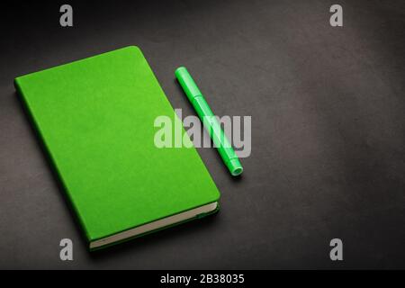 Green Notepad with a felt-tip pen on a black background, top view. Free space. Stock Photo