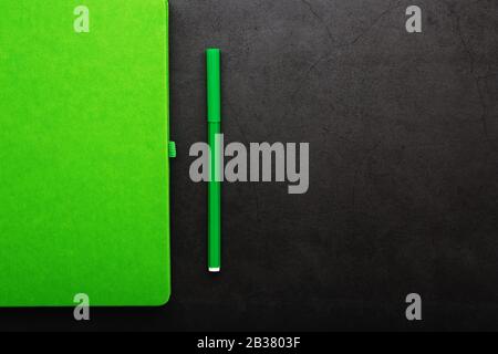 Green Notepad with a felt-tip pen on a black background, top view. Free space. Stock Photo