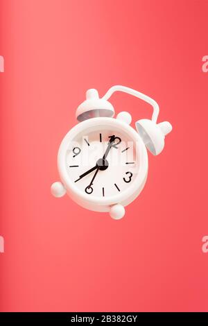 White retro style alarm clock in levitation isolated on pink background. Arrows on the time 7: 00. Minimalistic creative modern still life photography Stock Photo