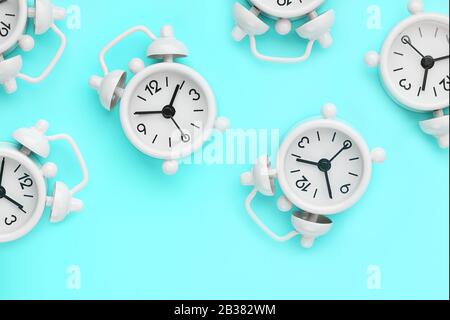 A pattern of many white classic alarm clocks in the form of a pattern on a blue background. Top view with a copy of the space, flat lay. Concept of sm Stock Photo