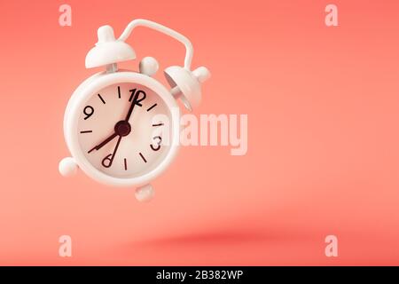 White alarm clock in levitation with shadow isolated on pink background. Hands on the clock 7. Minimalistic creative modern still life concept Stock Photo